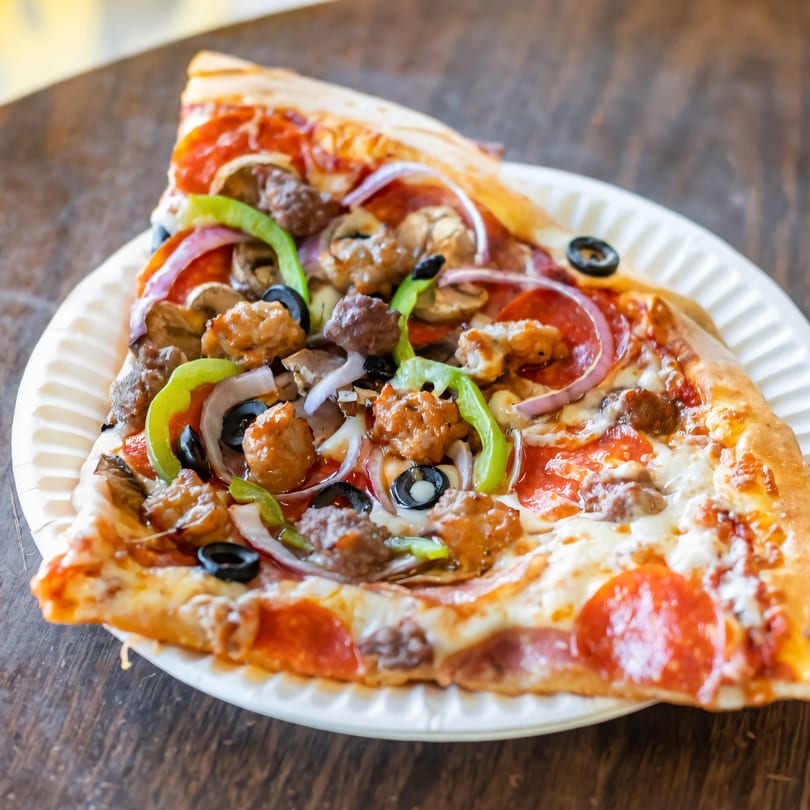 A large slice of New York Pizza with pepperoni, sausage, peppers, onions, mushrooms, and olives.