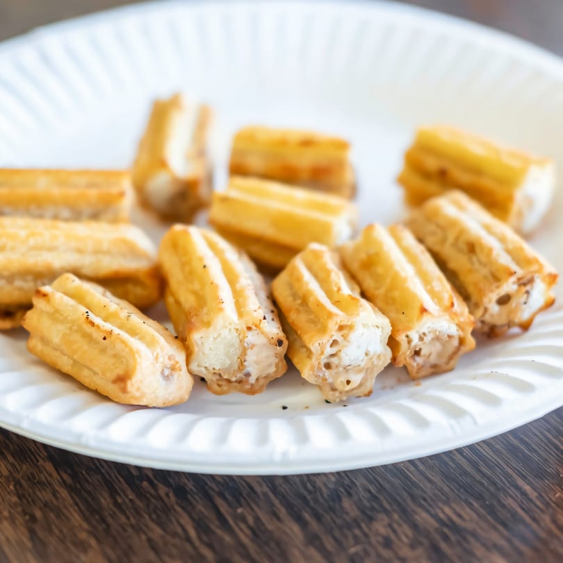 Golden-brown cheese sticks, some with visible melted cheese, arranged on a white paper plate.