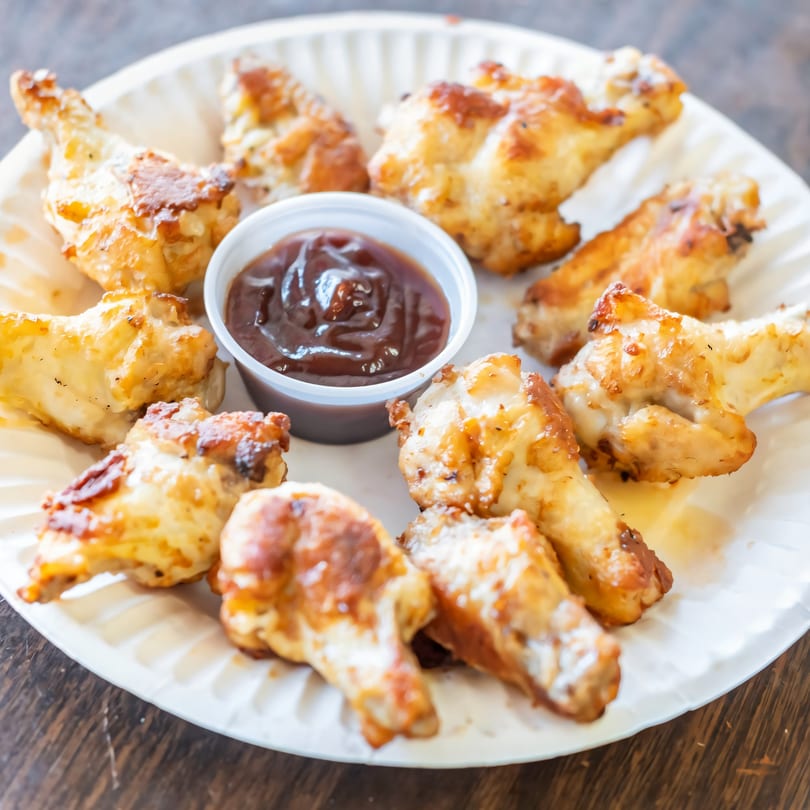 Golden-brown chicken wings with a side of barbecue sauce on a white paper plate.
