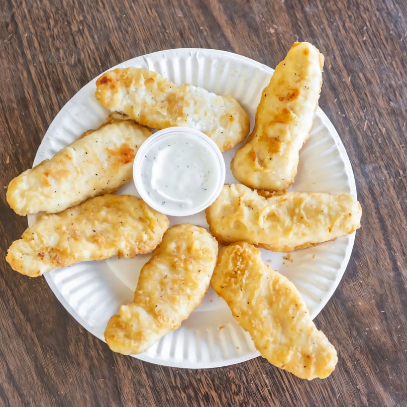 Golden-brown fried chicken tenders with a side of ranch dressing on a white paper plate.